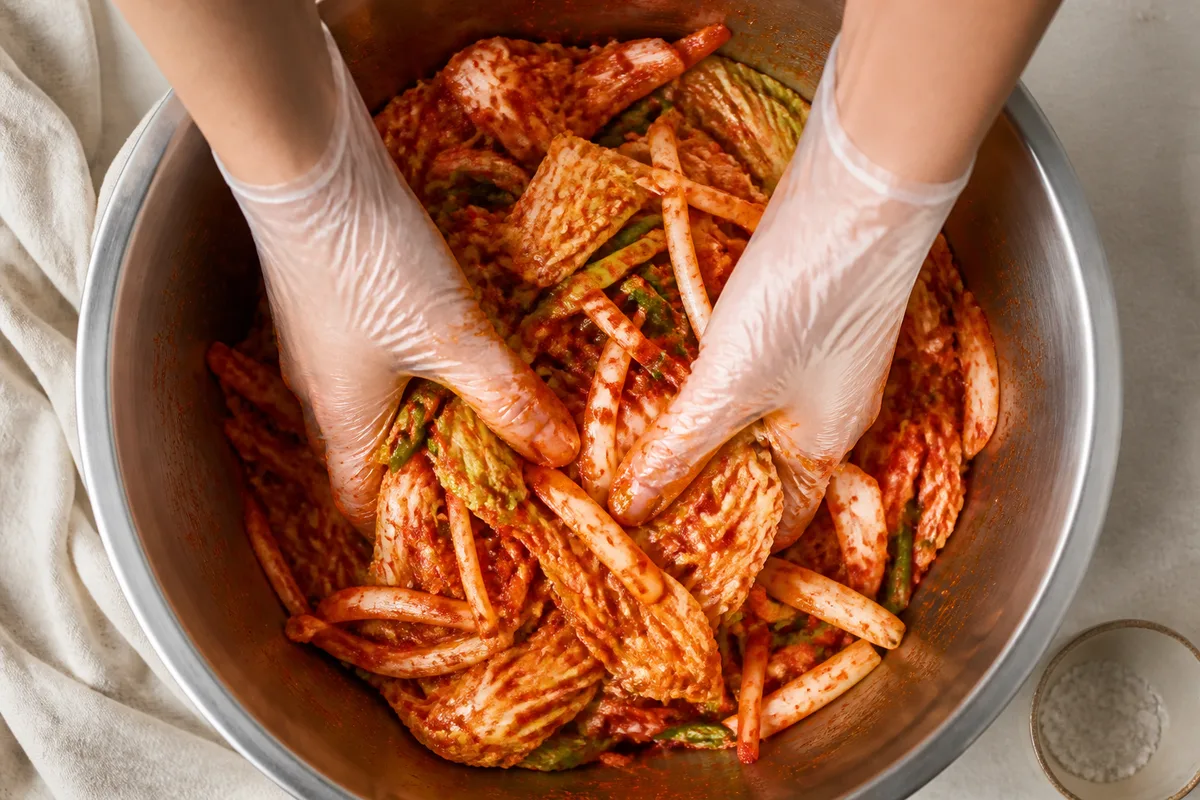 Mains gantées mélangeant du chou et du piment rouge dans un saladier